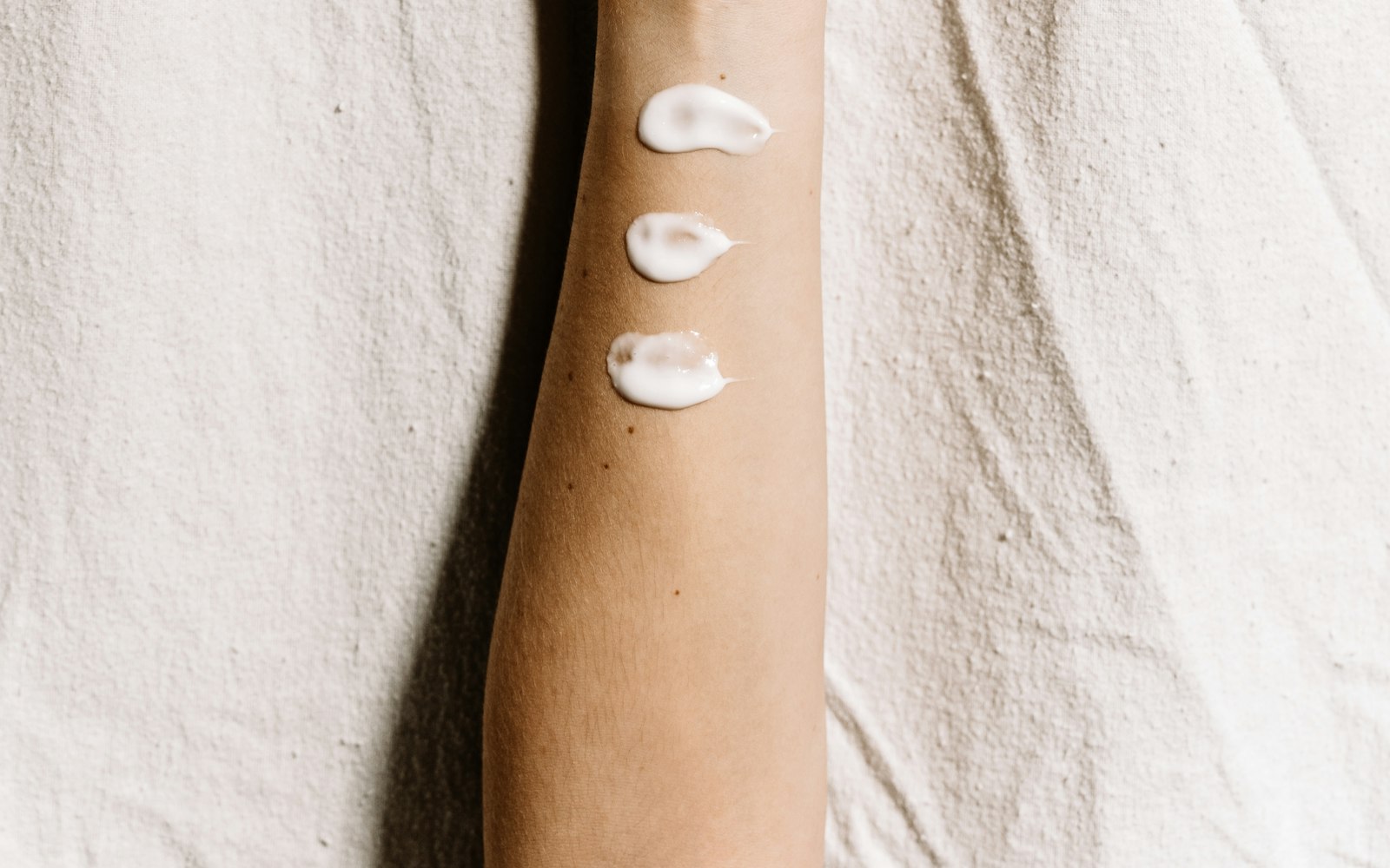 Three small dabs of white cream on an inner forearm for a patch test
